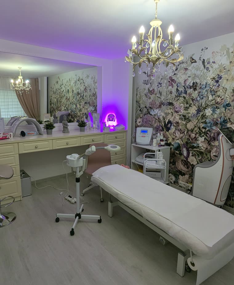 Cabinetul de tratamente faciale: patul, aparatul cu vapori și candelabrul, în fața tapetului cu flori